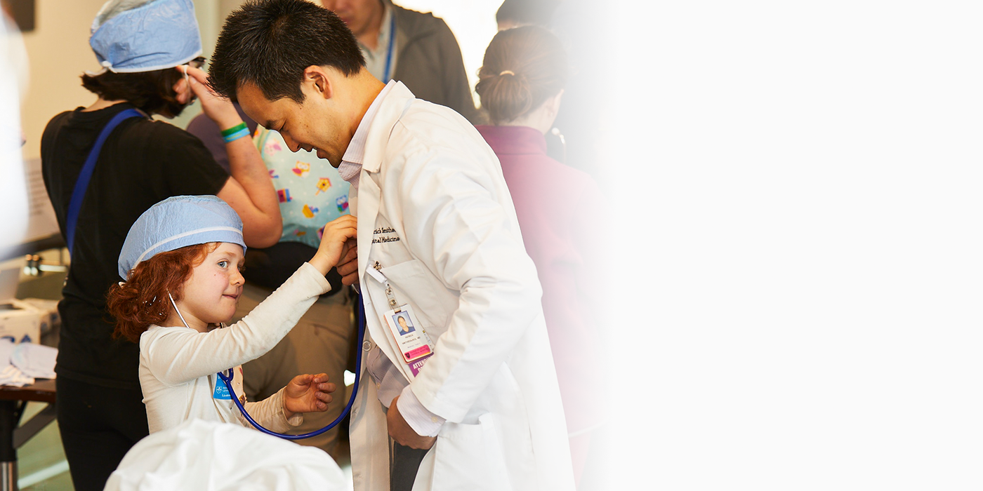 A child hold a stethoscope to a doctor's chest