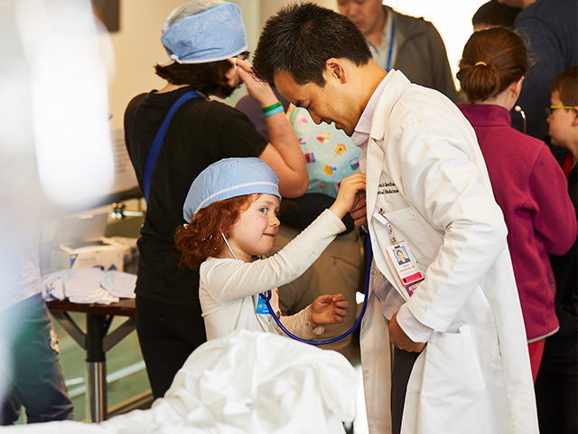 A child hold a stethoscope to a doctor's chest
