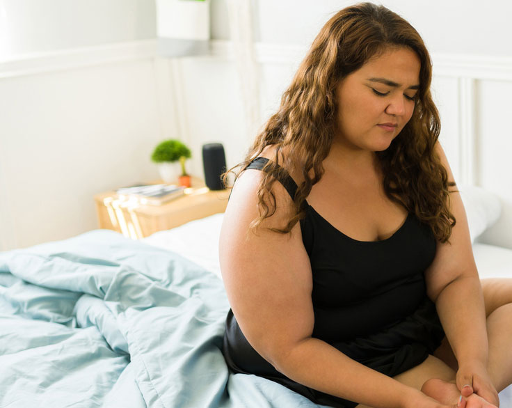 Woman rubbing her foot while sitting on a bed